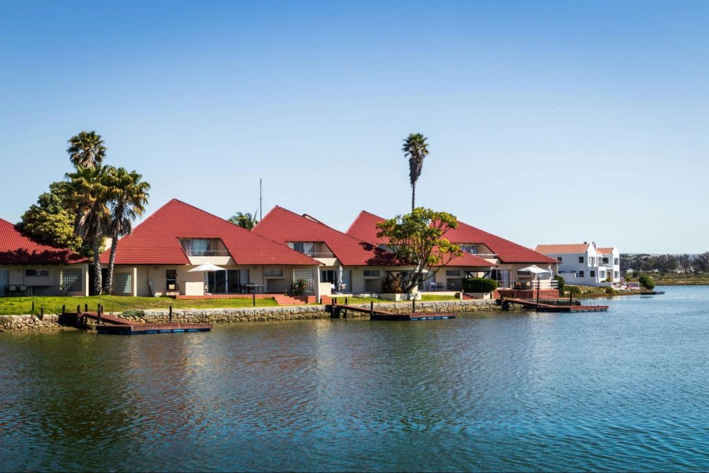 Vakantiewoningen met rode daken aan het waterfront, omgeven door palmbomen, als illustratie van recreatief vastgoed met verhuurpotentieel op een aantrekkelijke locatie.