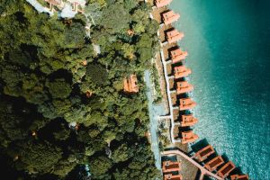 Luchtfoto van vakantiewoningen met oranje daken gelegen tussen bos en water, als voorbeeld van recreatief vastgoed op een toeristische locatie.
