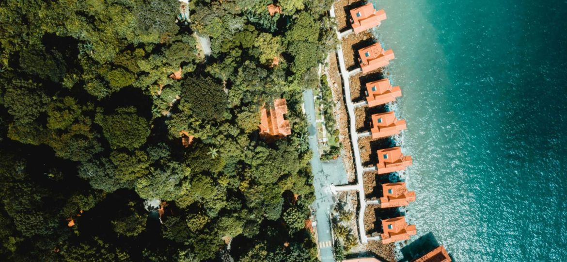 Luchtfoto van vakantiewoningen met oranje daken gelegen tussen bos en water, als voorbeeld van recreatief vastgoed op een toeristische locatie.