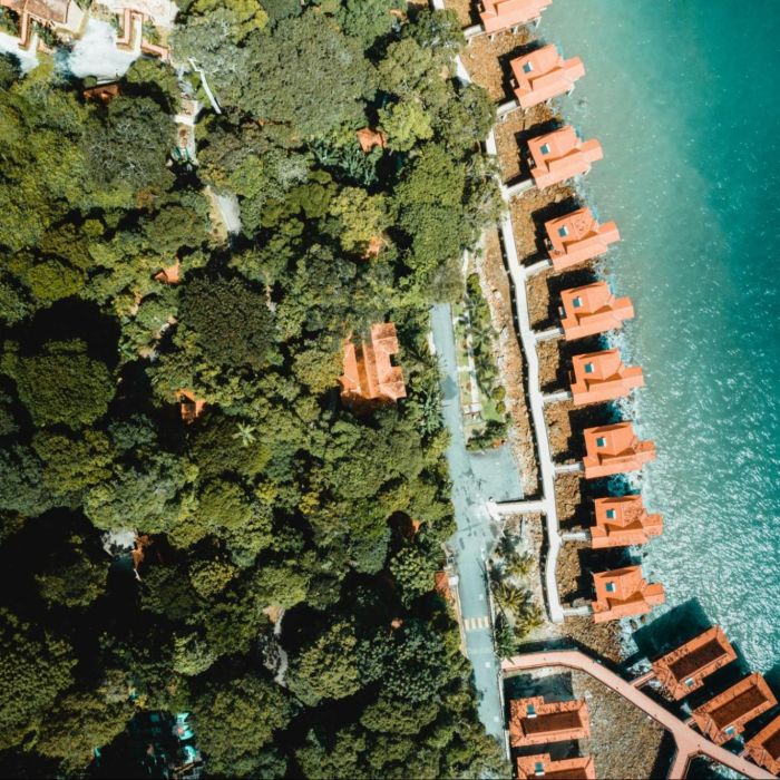Luchtfoto van vakantiewoningen met oranje daken gelegen tussen bos en water, als voorbeeld van recreatief vastgoed op een toeristische locatie.